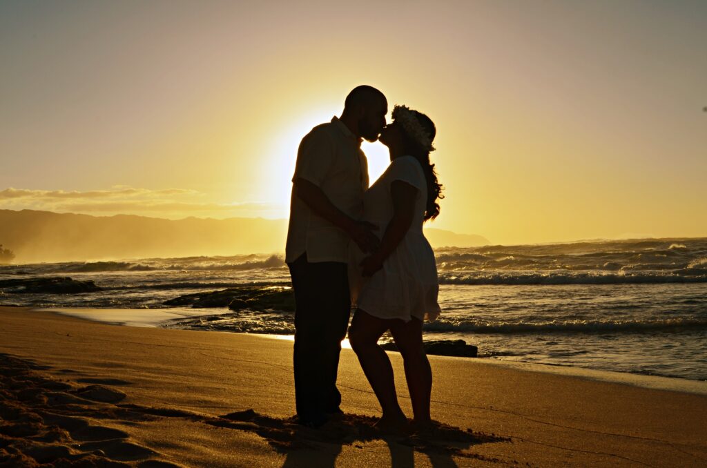 Pregnant couple kissing on a beach in Oahu, Hawaii during sunset in first maternity photography session