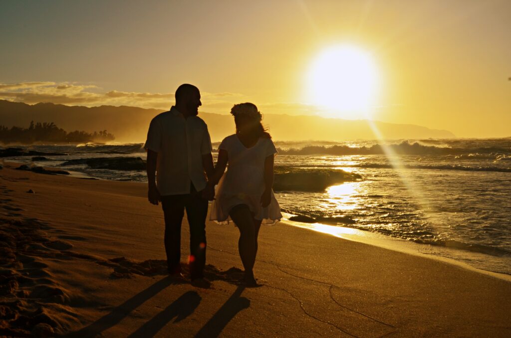 Couple walking on a beach in Oahu, Hawaii during sunset in first maternity photography session