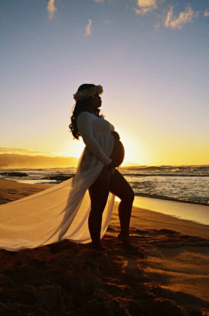 Pregnant mother posing in maternity dress on a beach during sunset in Oahu, Hawaii in first maternity photography session