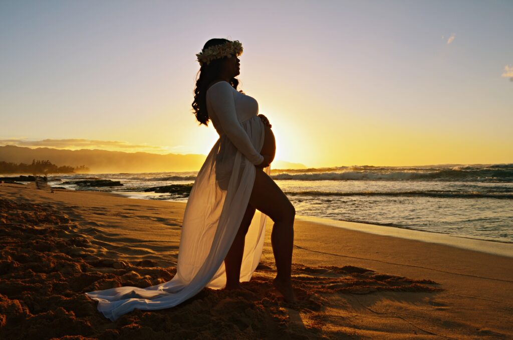 Pregnant mother posing in maternity dress on a beach during sunset in Oahu, Hawaii in first maternity photography session